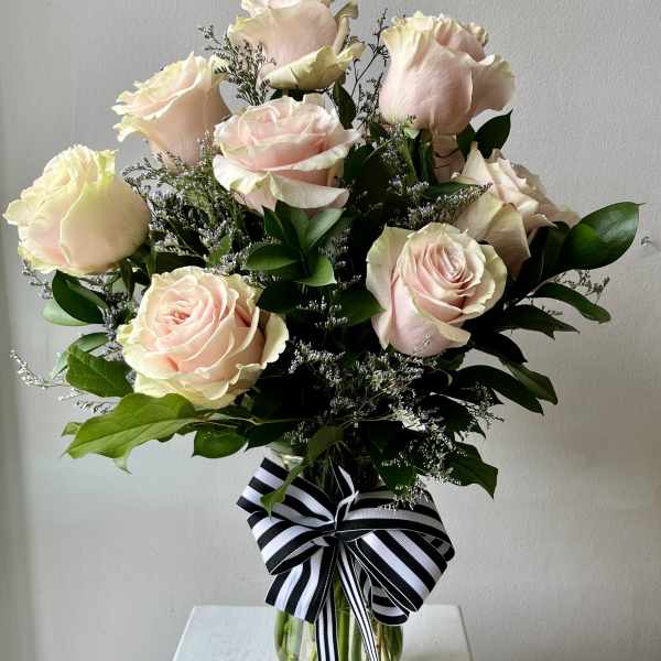 Bouquet of pale pink roses in a clear glass vase with a striped ribbon