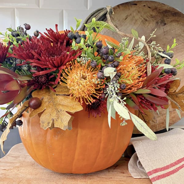 Fall floral arrangement in a pumpkin container with red and orange blooms
