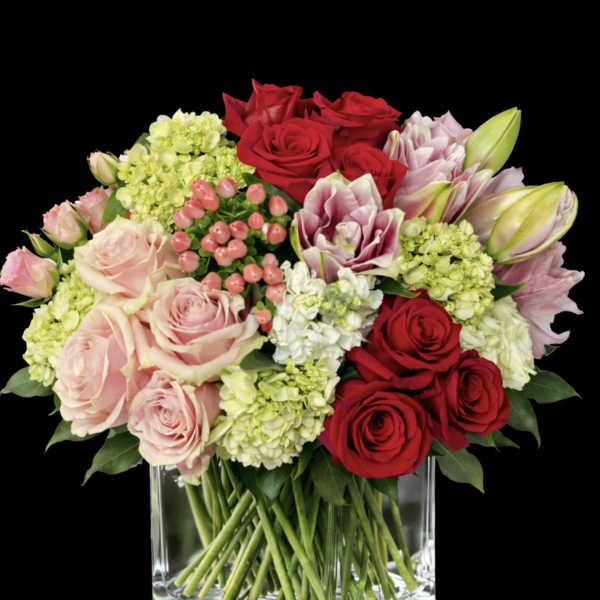 Bouquet of red and blush roses with pale hydrangeas in a clear glass vase