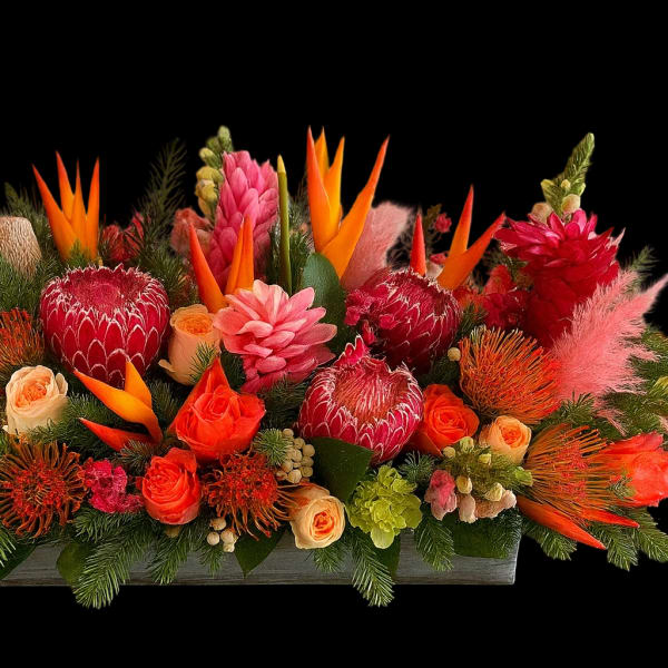 Bright tropical floral arrangement with red, orange, and pink blooms in a low rectangular container