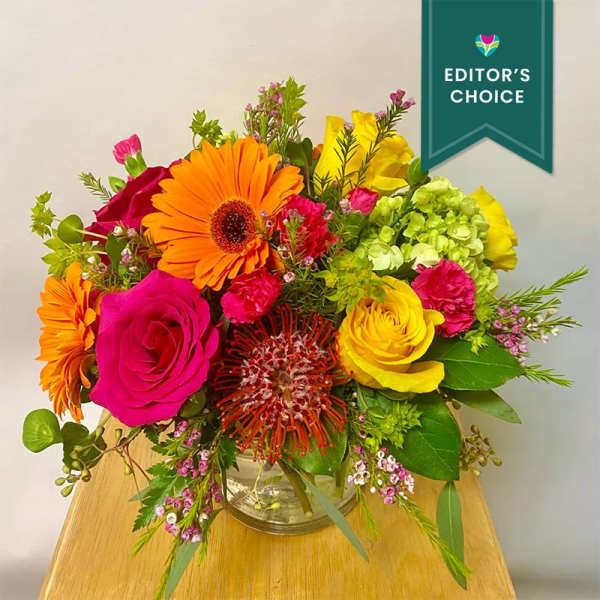 Bright mixed bouquet in a glass vase with orange, pink, yellow, and green blooms