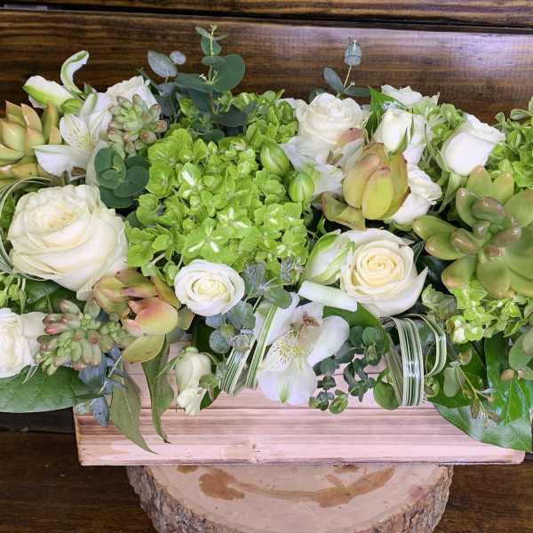 Low floral centerpiece with white roses, green hydrangeas, and succulents in a wooden box