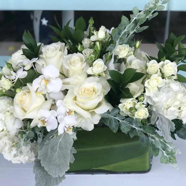 White rose and orchid arrangement in a green rectangular vase