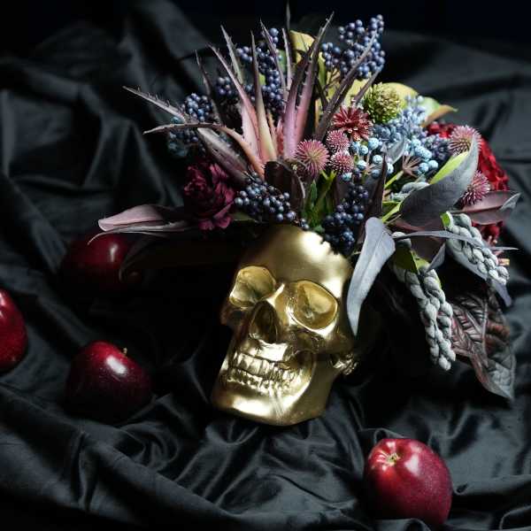 Gold skull decorated with dark flowers and berries on black fabric