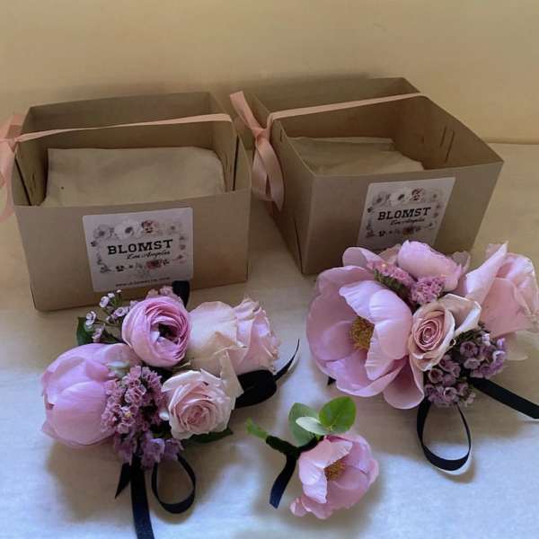 Pink floral boutonnieres and corsages with ribbon ties beside gift boxes