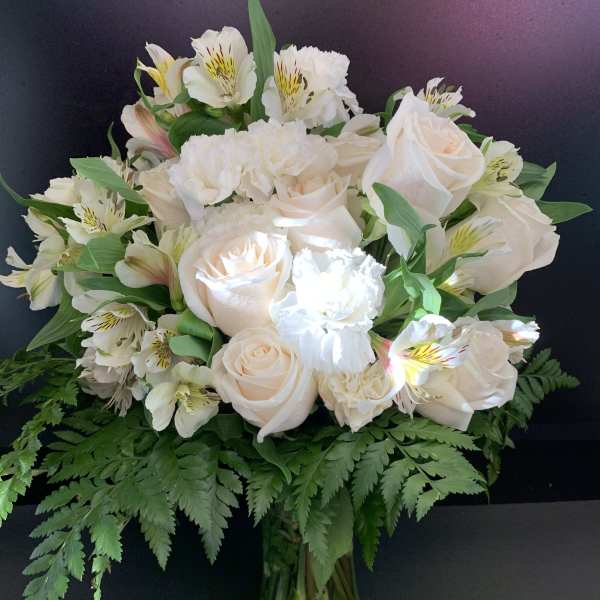 White roses and alstroemeria in a glass vase with fern foliage