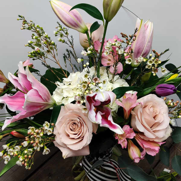 Bouquet of pink lilies, pale roses, and white filler flowers in a glass vase