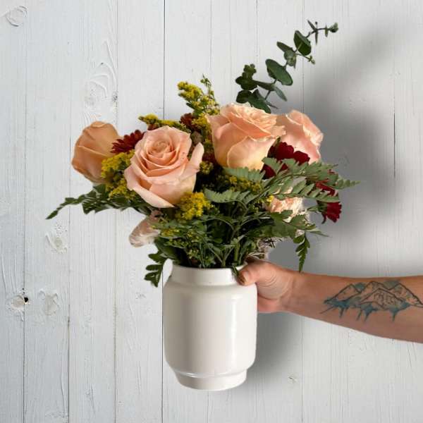 Peach roses in a white vase with mixed greenery and small accent blooms