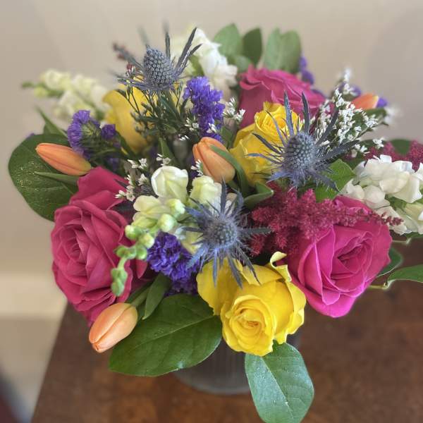 Bouquet of pink and yellow roses with purple thistle in a vase