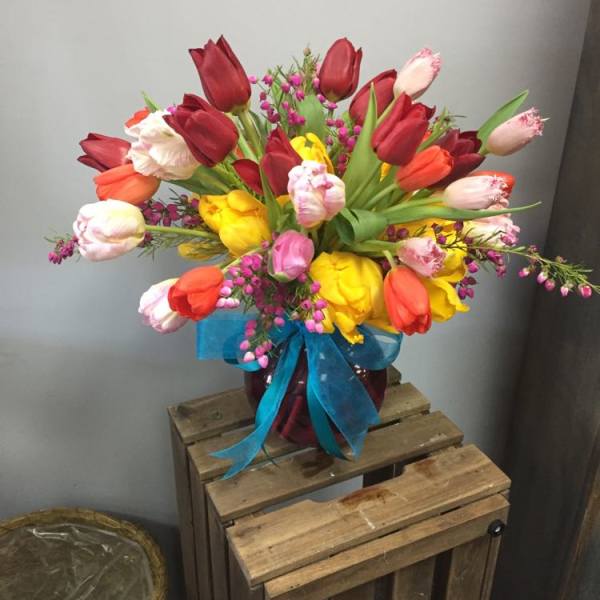 Colorful tulip bouquet in a glass vase with a blue ribbon