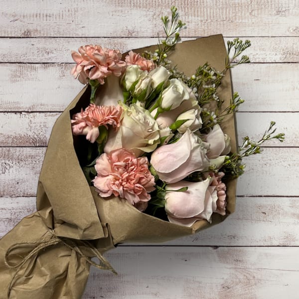 Bouquet of pale pink roses and carnations wrapped in brown paper