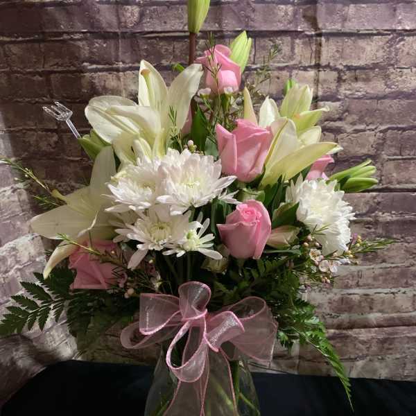 Pink roses and white lilies in a glass vase with a pink ribbon