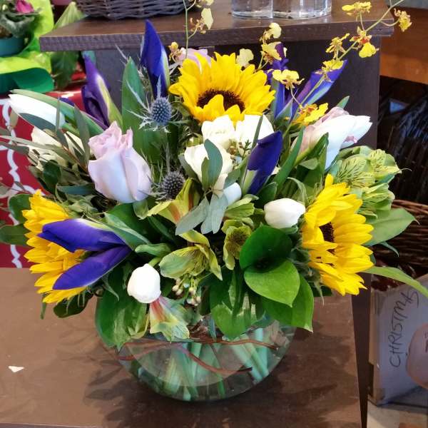 Mixed bouquet with sunflowers, purple tulips, and pale roses in a glass vase