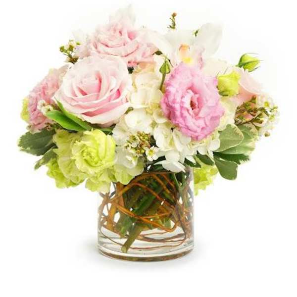 Low arrangement of pink roses and mixed pastel flowers in a clear glass vase with curly branches.