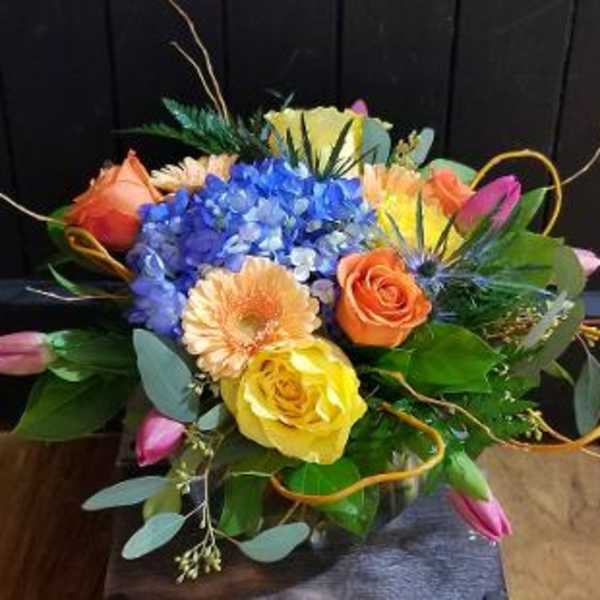 Colorful bouquet with blue hydrangea, roses, and tulips in a glass vase
