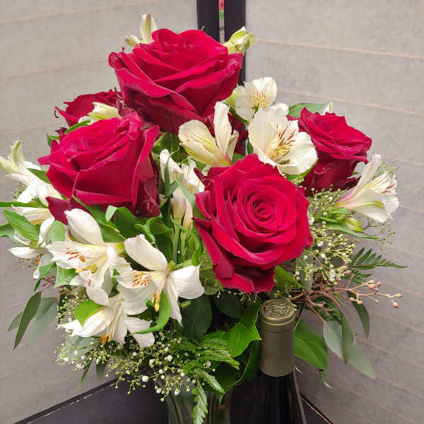 Bouquet of red roses and white alstroemeria in a glass vase with a wine bottle
