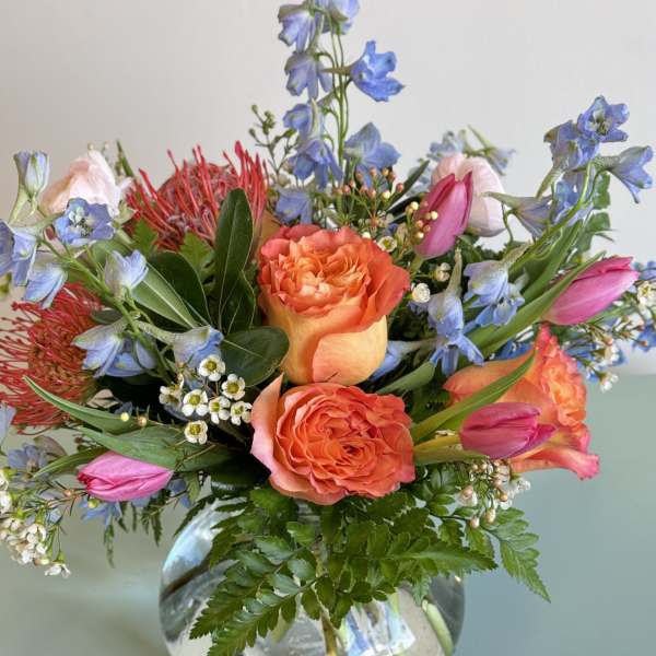 Bouquet of orange roses, pink tulips, and blue flowers in a glass vase