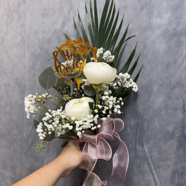 White floral bouquet in a glass vase with a pink ribbon and birthday topper