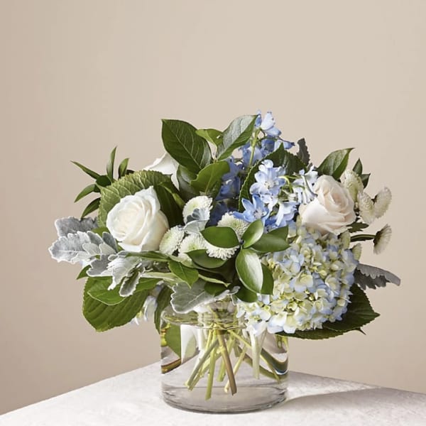 White roses and blue hydrangeas in a clear glass vase