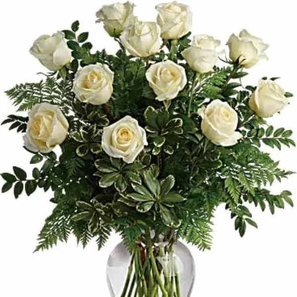 White roses arranged in a clear glass vase with greenery