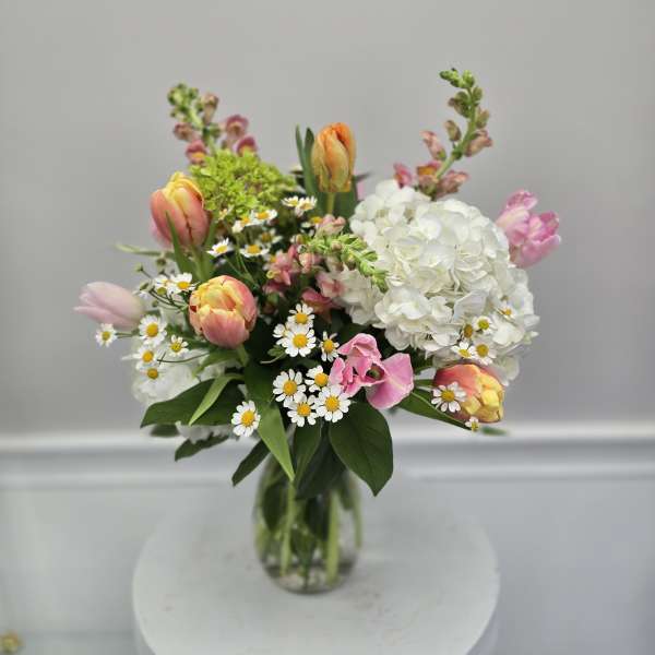 Mixed bouquet with tulips, white hydrangea, and small daisies in a glass vase