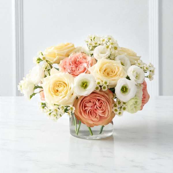 Low round arrangement of peach, cream, and white flowers in a clear glass vase