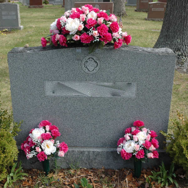 Pink and white floral arrangements on a gravestone in a cemetery