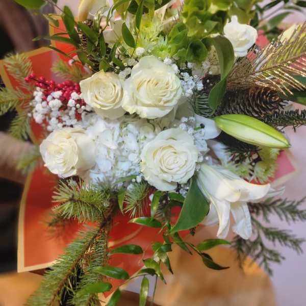 White roses and lilies arranged with greenery and pinecones