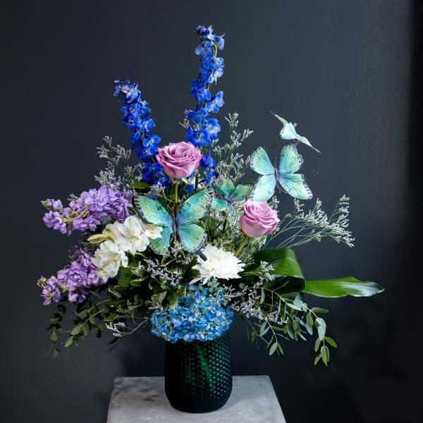 Tall floral arrangement with blue, purple, and white flowers in a dark vase