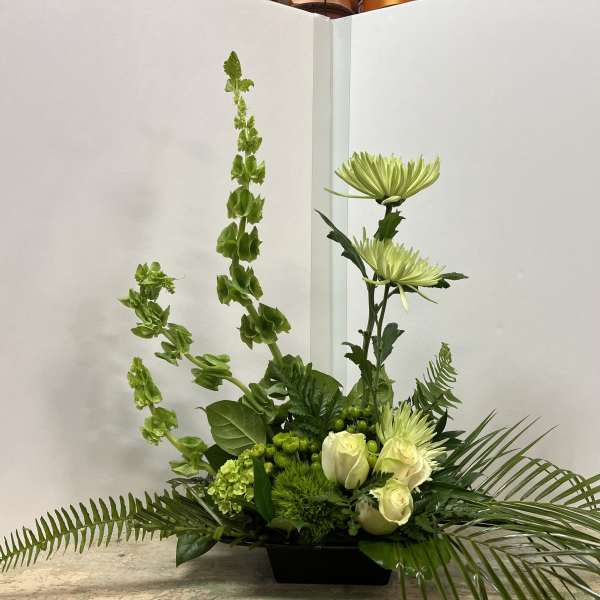 Green floral arrangement with white roses and tall spider mums in a black container