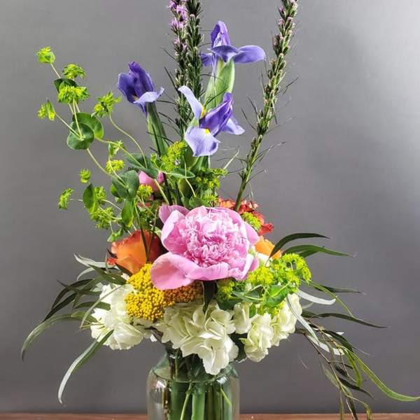 Tall mixed flower arrangement in a glass vase with pink, purple, white, and orange blooms