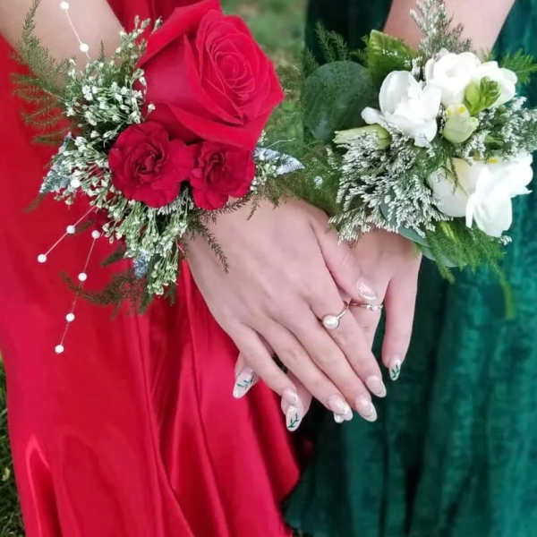 Two floral wrist corsages, one red and one white, worn on hands