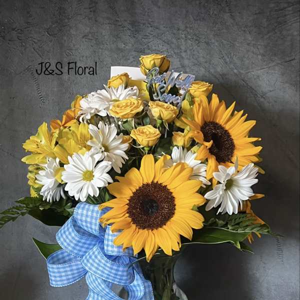 Bouquet of sunflowers, white daisies, and yellow roses in a glass vase with a blue ribbon