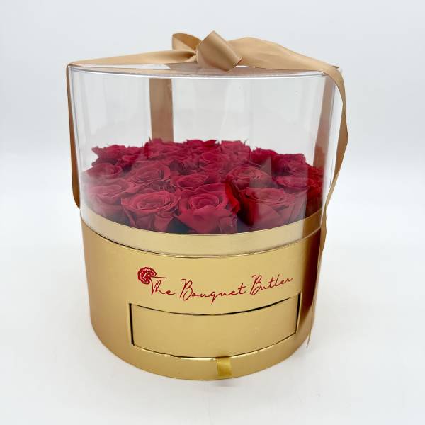 Red roses in a clear round gift box with a gold ribbon