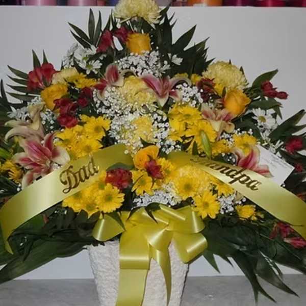 Large mixed flower arrangement with yellow ribbon in a white basket