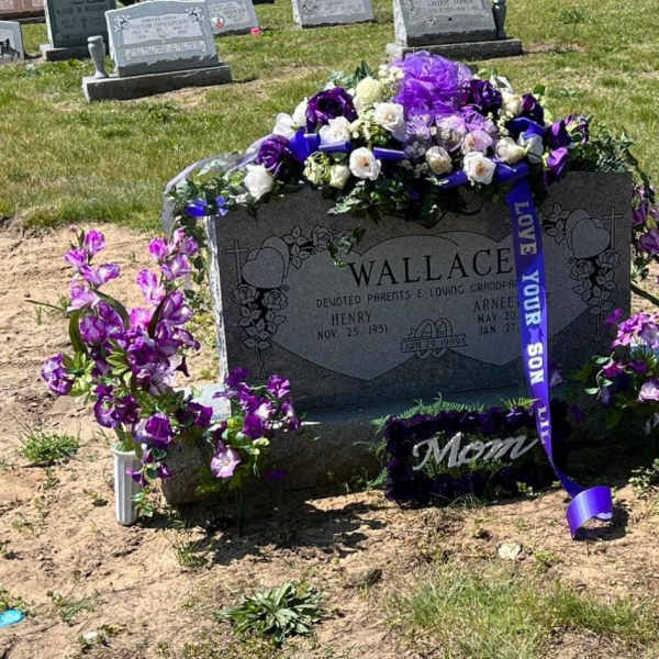 Purple and white floral tribute arranged on a gravestone with a ribbon