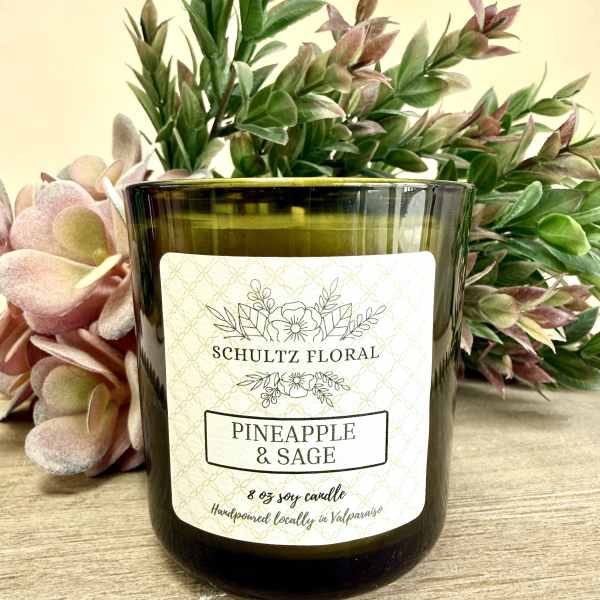 Green glass pineapple and sage candle with decorative foliage behind it