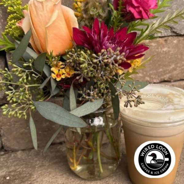 Bouquet of peach and magenta flowers in a glass vase beside a lidded iced drink