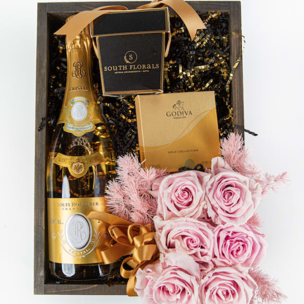 Wooden gift box with champagne, gold chocolate box, and pink roses tied with ribbon