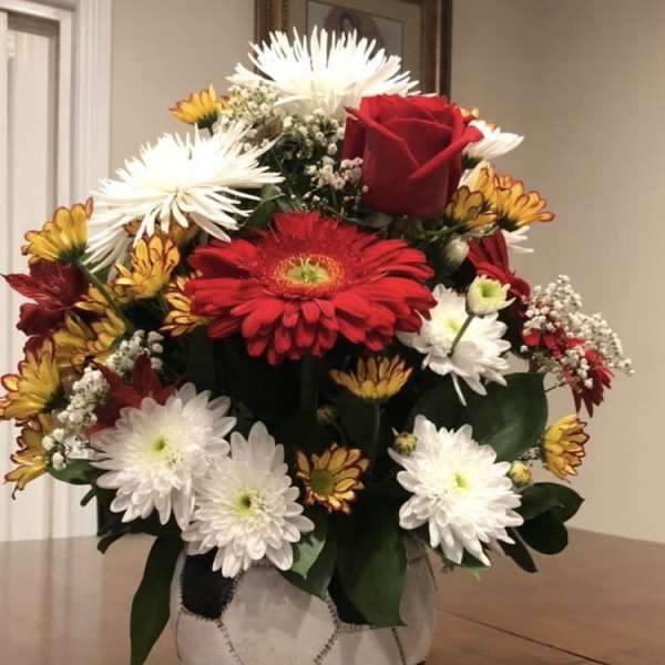 Bouquet of red roses and white daisies in a soccer ball vase