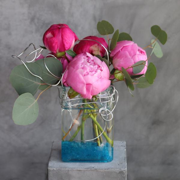 Pink peonies in a clear glass vase with eucalyptus and wire accents