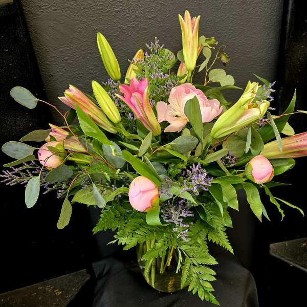 Pink lilies and peonies arranged in a glass vase with greenery.