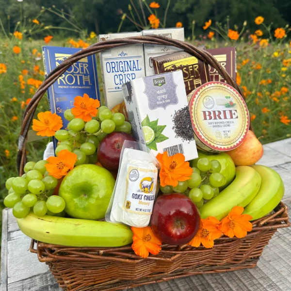 Wicker gift basket filled with fruit, cheeses, snacks, and orange flowers.