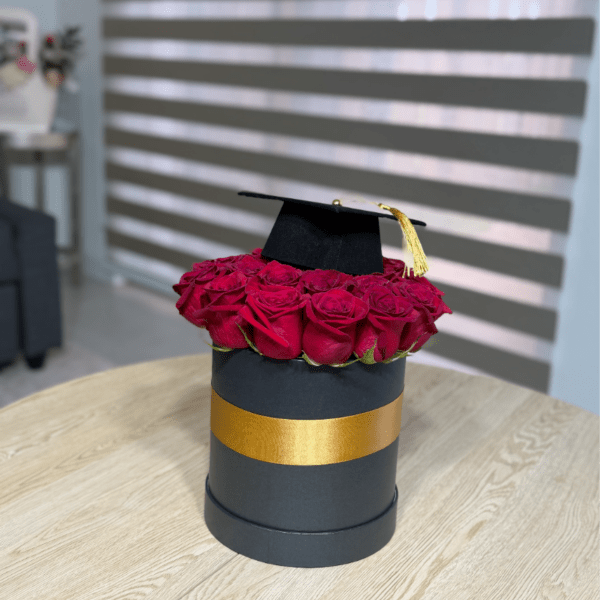 Red roses arranged in a black hat box with a graduation cap on top