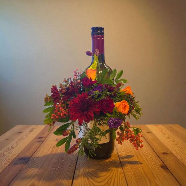 Flower arrangement wrapped around a wine bottle on a wooden table
