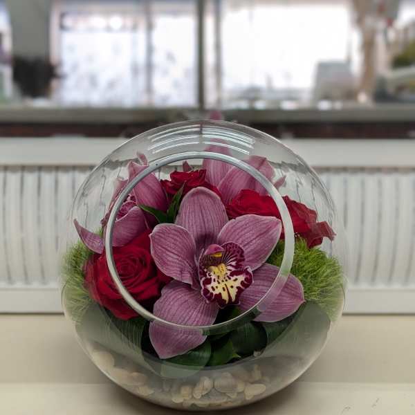 Pink orchids and red roses in a clear round glass vase