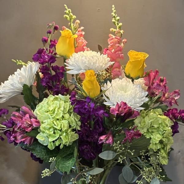 Mixed bouquet of yellow roses, white mums, and pink and green blooms in a clear glass vase