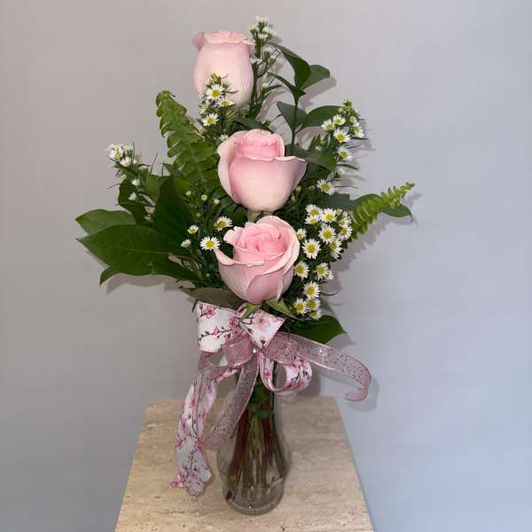 Pink roses arranged in a clear glass vase with small white daisies