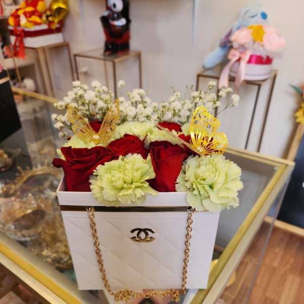 Red roses and pale green carnations in a white box with gold chain handles
