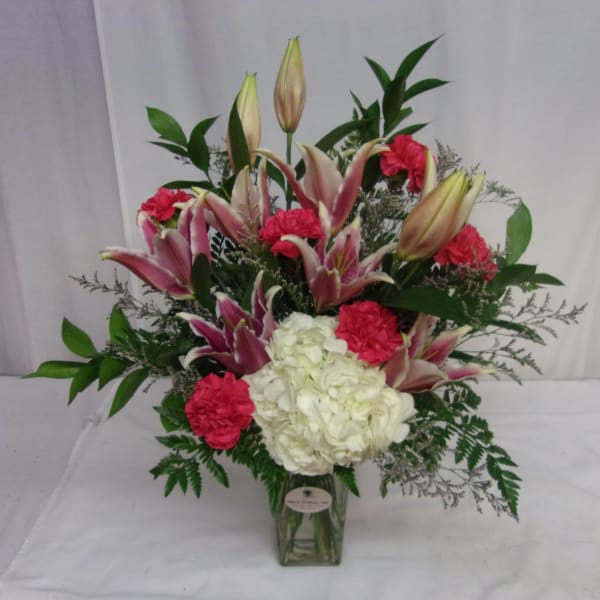 Pink lilies and red carnations in a glass vase with white hydrangea